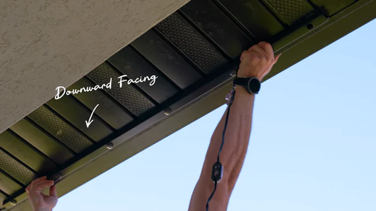 Title: EverLights ClickLights RGBW - Description: Installer holding an EverLights ClickLights channel beneath a soffit, with the manufacturer’s Downward Facing arrow identifying the light orientation.